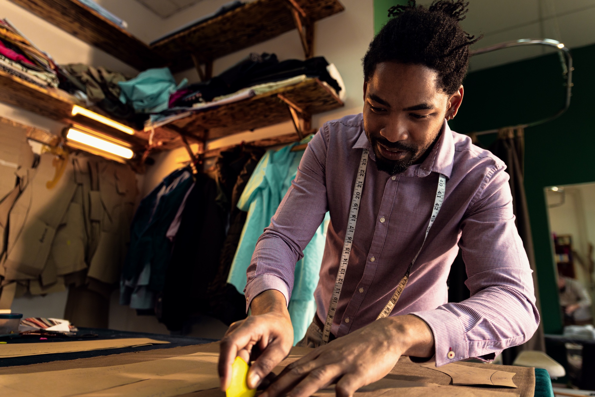 Male fashion tailor working on the measurements for the suit design in his workshop.